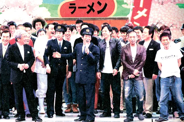 吉本興業100周年公演「伝説の一日」で、2012年に上演された「さんまの駐在さん」の舞台上に勢揃いした明石家さんま、ダウンタウン、桂文枝ら同社の売れっ子タレント。左端には当時の大﨑洋社長の姿が見える=「吉本興業百五年史」から